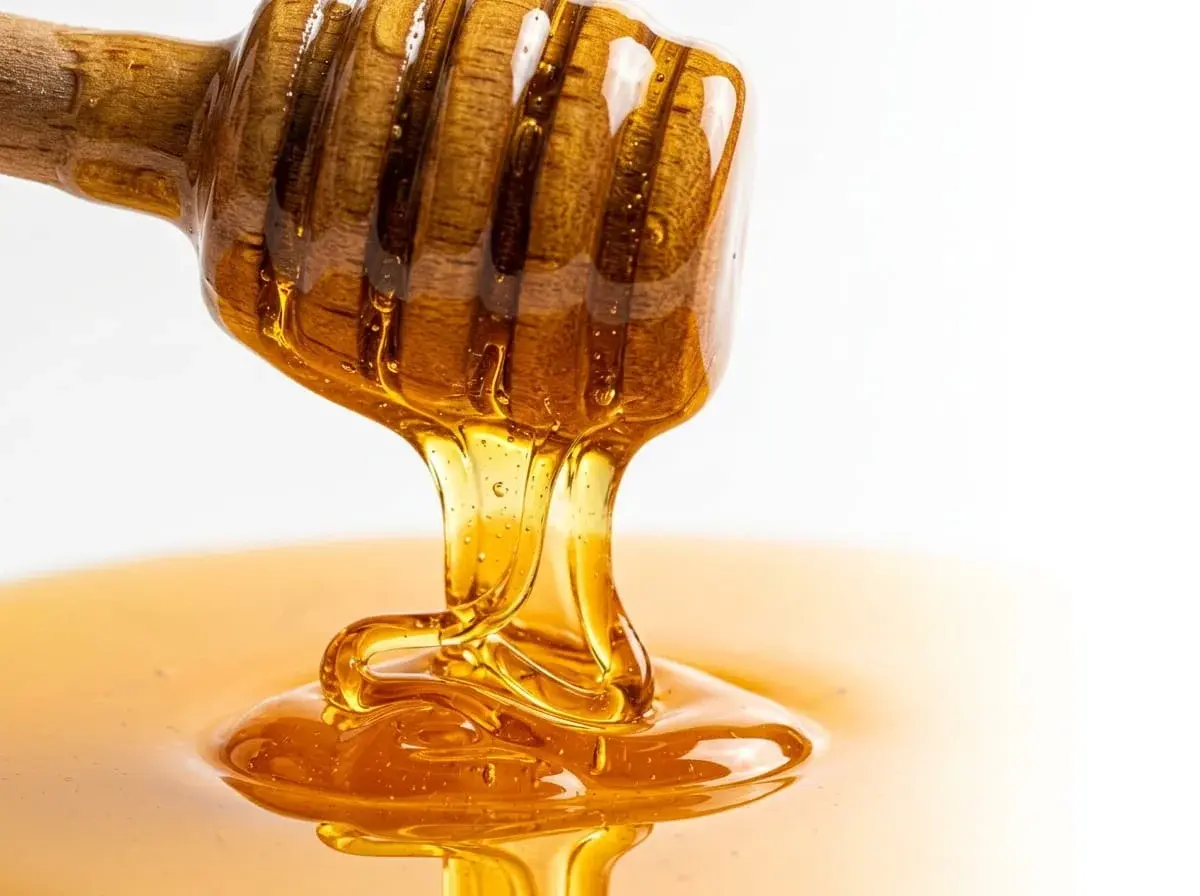Golden honey dripping from a wooden dipper
